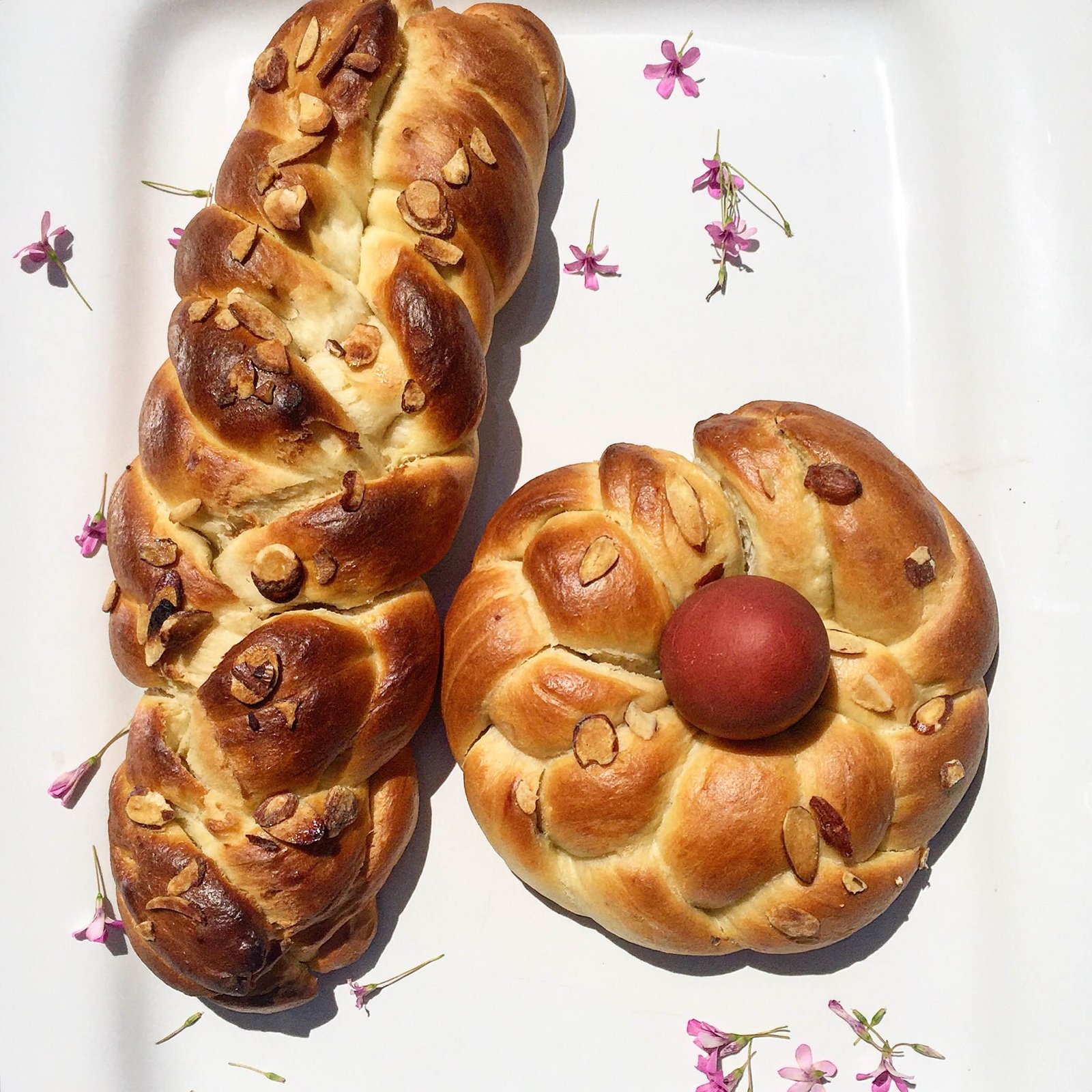 A photo of two tsoureki loaves one being round with a red egg and the other long and braided. 