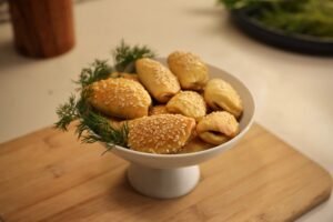 A bowl of the tasty mini olive pies with dill surrounding it.
